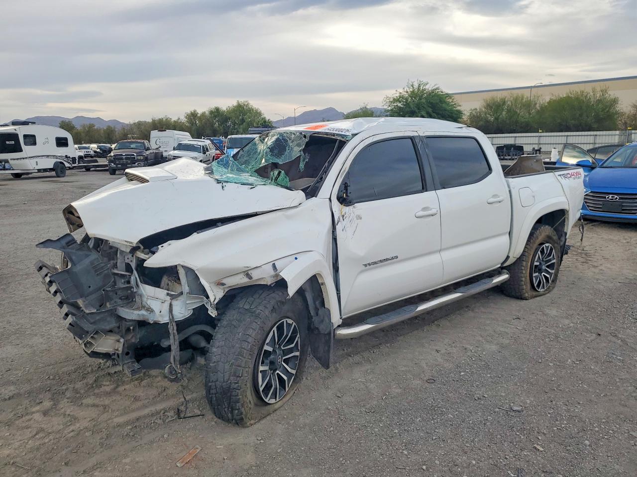 A white 2020 Toyota Tacoma TRD Sport pickup with front-end and roof collision damage at a salvage yard