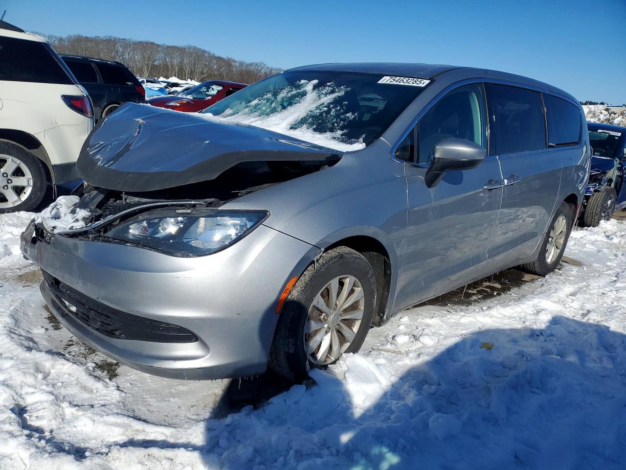 A silver 2017 Chrysler Pacifica Touring minivan with front-end collision damage in a snowy salvage yard