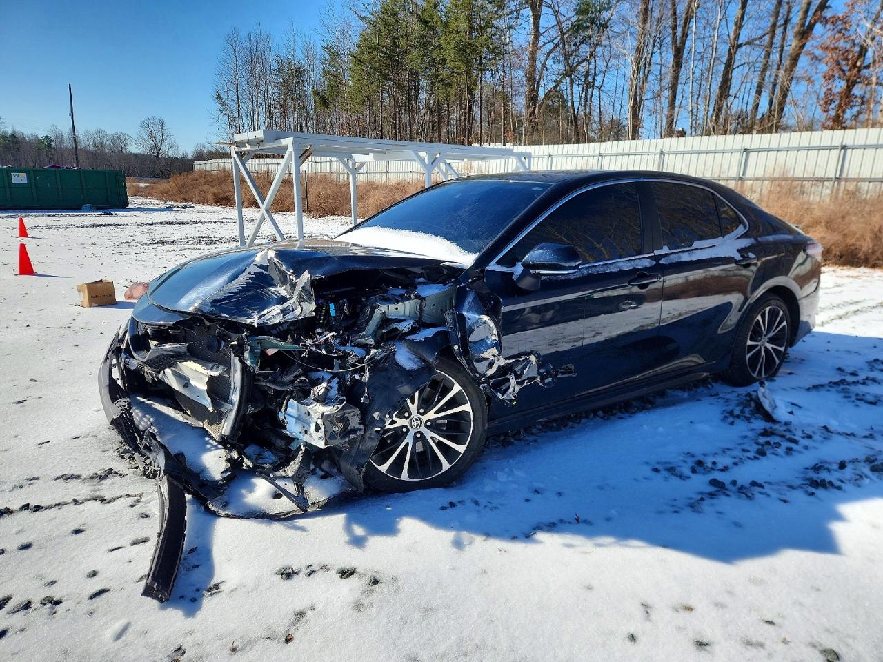 A dark blue 2020 Toyota Camry SE with severe front-end collision damage in a snowy salvage yard