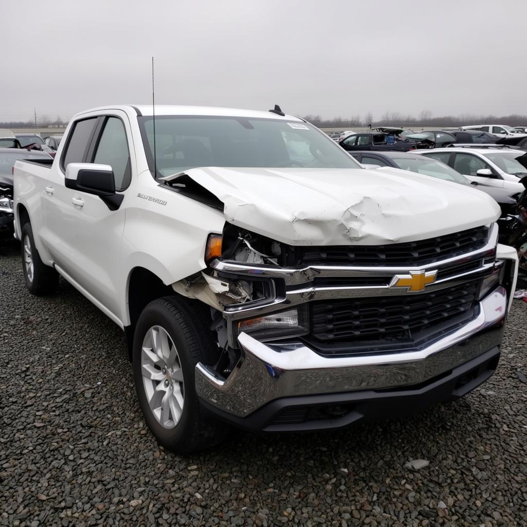 A white 2020 Chevrolet Silverado 1500 LT Crew Cab pickup with severe front-end collision damage at a salvage yard