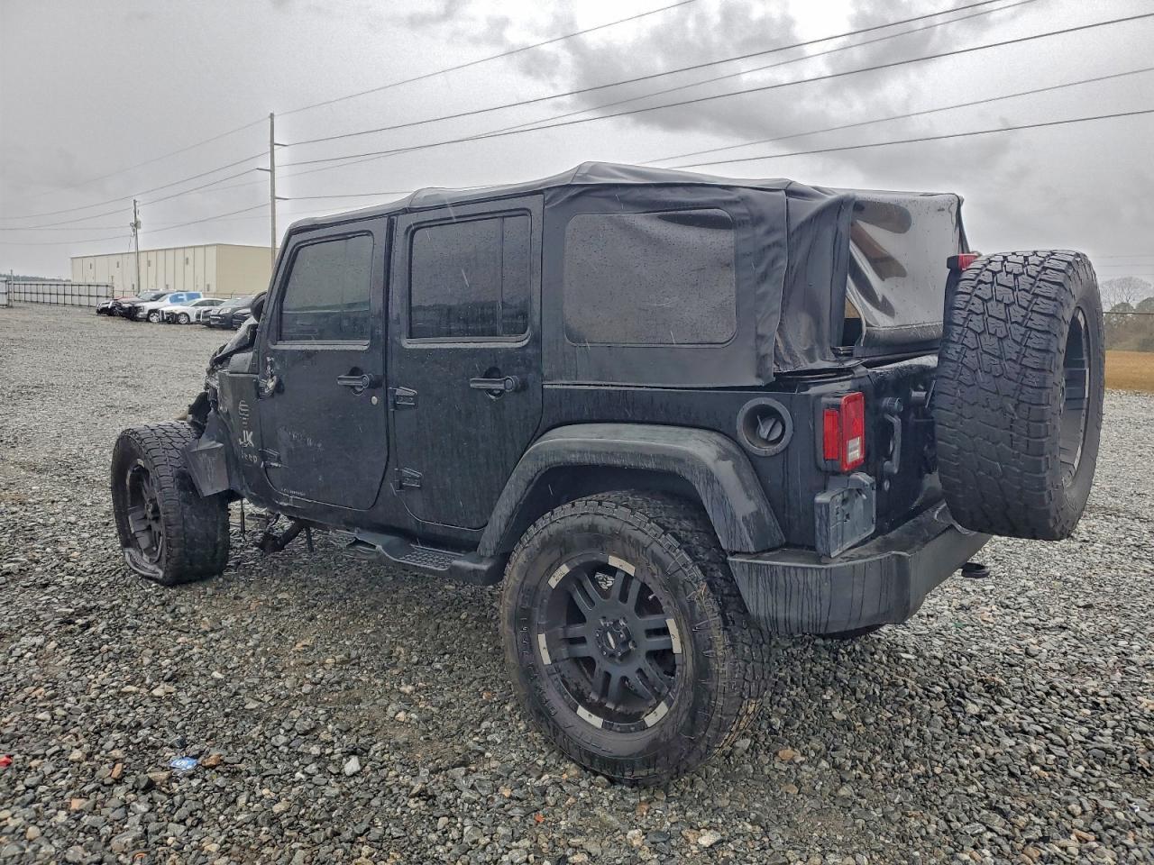 A bright red 2021 Jeep Wrangler Unlimited Sahara with hood lifted showing front-end collision damage at a body shop