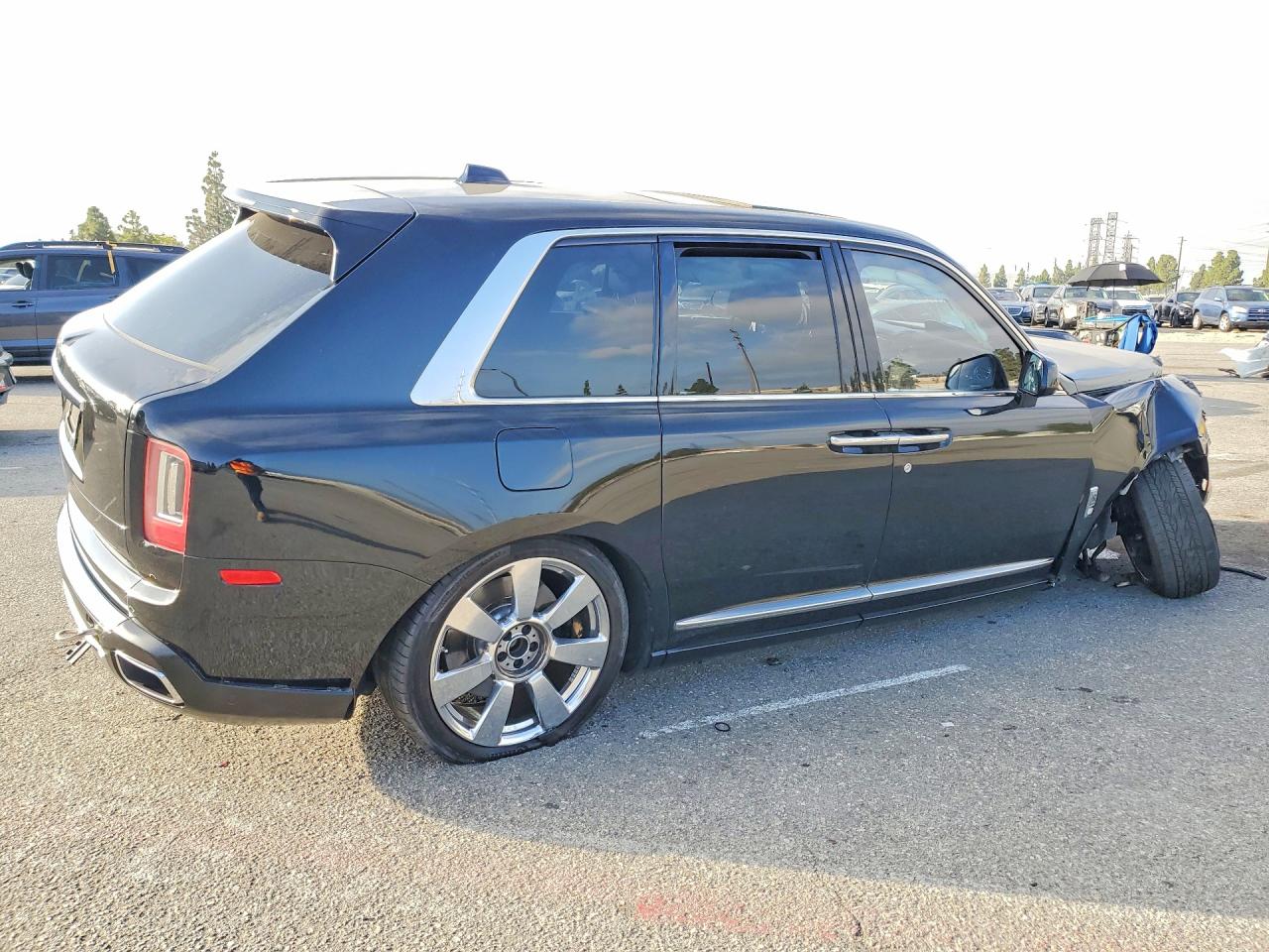 A white Rolls-Royce Cullinan SUV with rear-end collision damage parked in a salvage yard